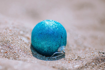 Blue shiny Christmas ball on white sand.