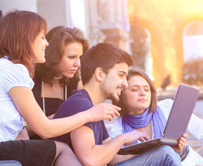 Cheerful group of students smiling and looking at a laptop.