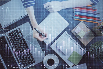 Financial forex graph drawn over hands taking notes background. Concept of research. Double exposure