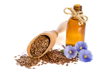 Flax seeds in the wooden scoop, bottle with oil and  beauty flowers isolated on white background.