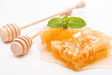 sweet honeycomb with honey and mint near wooden honey dippers on white background