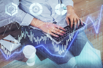 Double exposure of stock graph with businessman typing on computer in office on background. Concept...