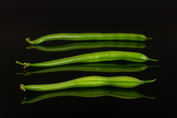 Group of three whole fresh green bean in row isolated on black glass