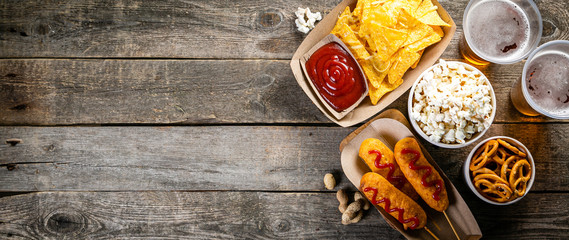 Selection of stadium game foods - nachos, pop corn, pretzels, corn dogs, rustic wood background