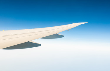 Wing of plane over white clouds. Airplane flying on clear blue sky. Scenic view from airplane window. Commercial airline flight. Plane wing above cloud. Flight mechanics concept. International flight.