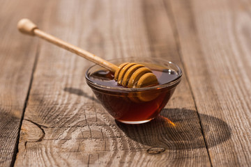 Fototapeta premium glass bowl with honey and honey dipper on wooden table in sunlight