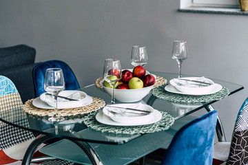 Arranged kitchen table for four people with fruits, glasses and plates with four colorful and vintage chairs