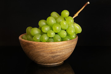 Lot of whole fresh green grape in big wooden bowl isolated on black glass