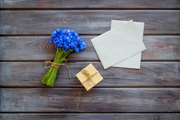 Bouquet of blue cornflowers, envelopes and box with present on wooden background top view mockup