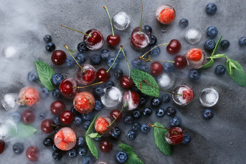 Flatlay of mint, various berries, ice and smoke on dark background, selective focus
