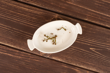 Group of two pieces of fresh green grape in white oval ceramic bowl flatlay on brown wood