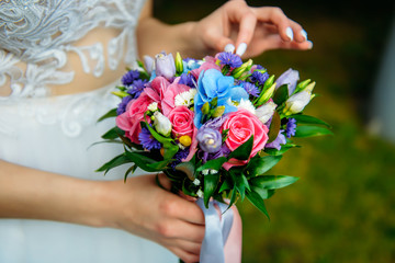Obraz na płótnie Canvas Stylish bride in a white dress holds an unusual wedding bouquet close-up. Delicate wedding bouquet of different flowers in the hands of the bride, selective focus.