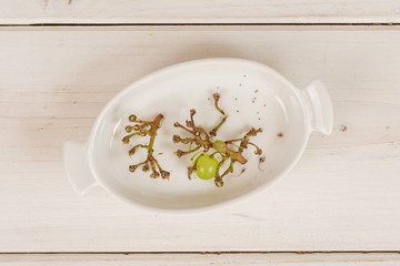 Group of two pieces of fresh green grape in white oval ceramic bowl flatlay on white wood