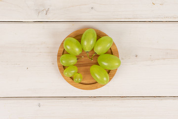 Lot of whole fresh green grape on round bamboo coaster flatlay on white wood