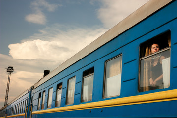 Girl on train. Portrait of passenger in window of blue railway car. Traveling alone by rail. Train in perspective