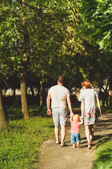 young lovely couple with a little kid, holding hands and walking together in a sunny warm summer day in a city park 
