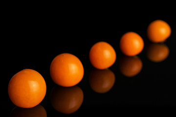 Group of five whole fresh orange physalis without husk placed diagonally in line isolated on black glass