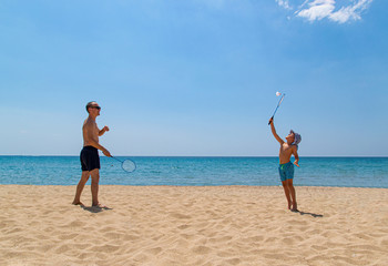 Father and son play with badminton racket and shuttlecock on the beach. The concept of a family holiday. Bright Sunny day on the beach.