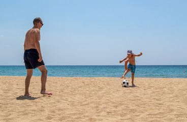 Father and son play football on the beach. The concept of sport and healthy lifestyle.Fresh sea air and good ecology. Friendship between father and son.