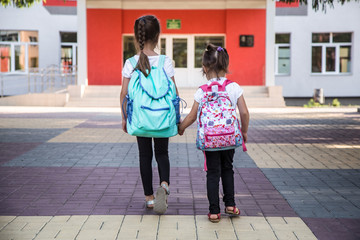 Back to school education concept with girl kids, elementary students, carrying backpacks going to class