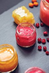 Creamed honey in jar with berries and fruits, dipper on black stone background
