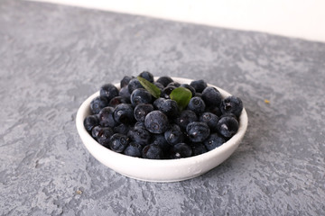 Bowl of tasty fresh blueberries, leaves on grey stone surface, flat lay