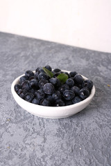 Bowl of tasty fresh blueberries, leaves on grey stone surface, flat lay. Space for text