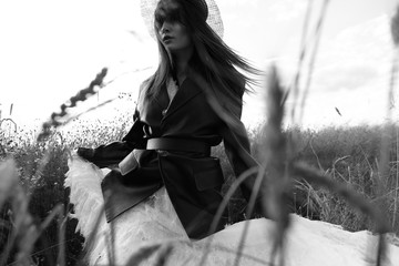 Black and white portrait of beautiful young woman in leather jacket, black hat, white dress., walking in grass.