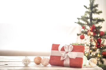 Red Christmas present over Christmas lights and Christmas tree on light background on cozy rug. Christmas decorations