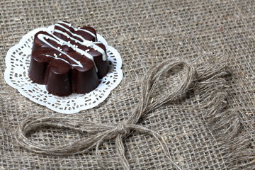 Chocolate dessert in the shape of a flower. Dark chocolate coated. Garnished with white chocolate and sprinkles. On coarse linen cloth.