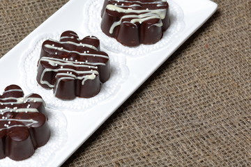 Chocolate dessert in the shape of a flower. Dark chocolate coated. Garnished with white chocolate and sprinkles. On coarse linen cloth.