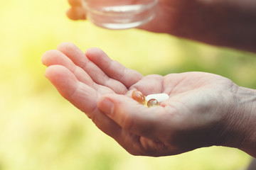 senior woman's hands holding glass of water and assorted colorful medicine pills