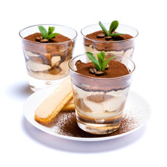 Classic tiramisu dessert in a glass cup and savoiardi cookies on plate with spoon isolated on a white with clipping path