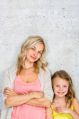 pretty, blonde young mother poses and cuddles with her daughter in front of a concrete wall and...