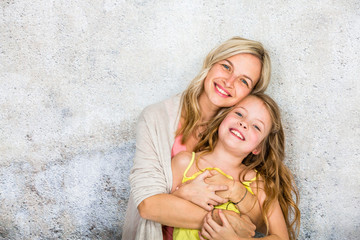 pretty, blonde young mother poses and cuddles with her daughter in front of a concrete wall and having a lot of fun