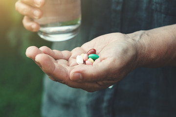 senior woman's hands holding glass of water and assorted colorful medicine pills