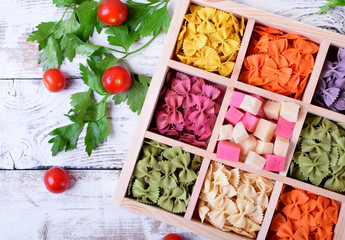 Multicolored pasta farfalle and cubes of cheese in wooden box