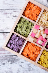 Multicolored pasta farfalle and cubes of cheese in wooden box