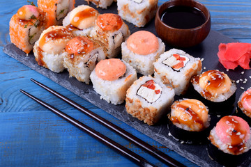Sushi rolls assortment served on slate plate and chopsticks on blue table
