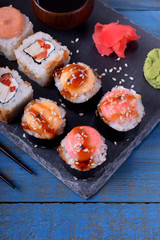 Sushi rolls assortment served on slate plate and chopsticks on blue table