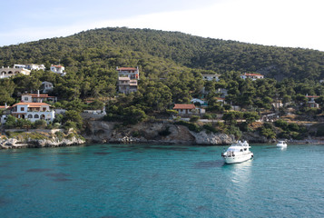 Naklejka premium Greece, the pine clad island of Angistri. Pleasure boats near the rocky shore. Holiday villas on the hillside.