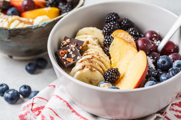 Oatmeal with banana, peach, berries and superfoods in bowls.