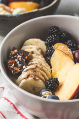 Oatmeal with banana, peach, berries and superfoods in bowls.