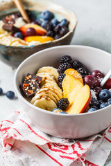 Oatmeal with banana, peach, berries and superfoods in bowls.