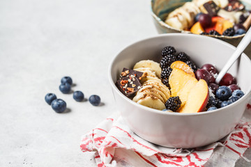 Oatmeal with banana, peach, berries and superfoods in bowls.