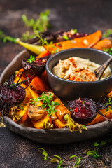 Baked vegetables with hummus in a dark dish.