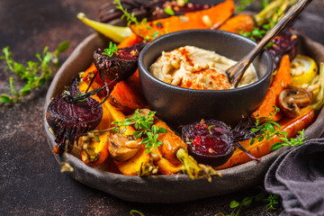 Baked vegetables with hummus in a dark dish.