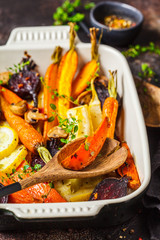 Baked vegetables with thyme in the oven dish, dark background.