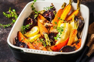 Baked vegetables with thyme in the oven dish, dark background.