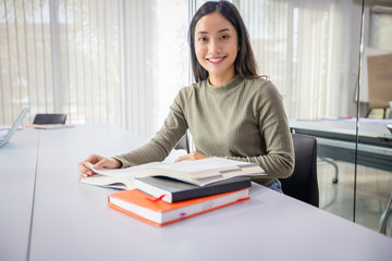 Asian women Students Smile and reading book and using notebook for helps to share ideas in the work and project. And also review the book before the exam